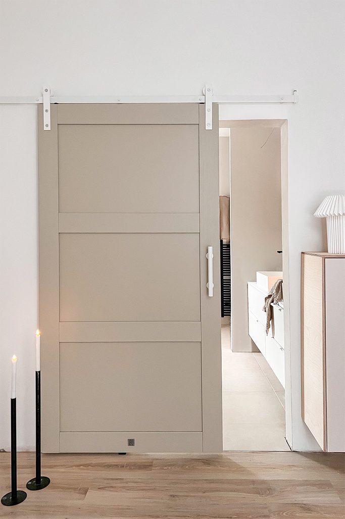 otwarte szaro-beżowe drzwi przesuwne z białym systemem przesuwnym ukazujące fragment łazienki