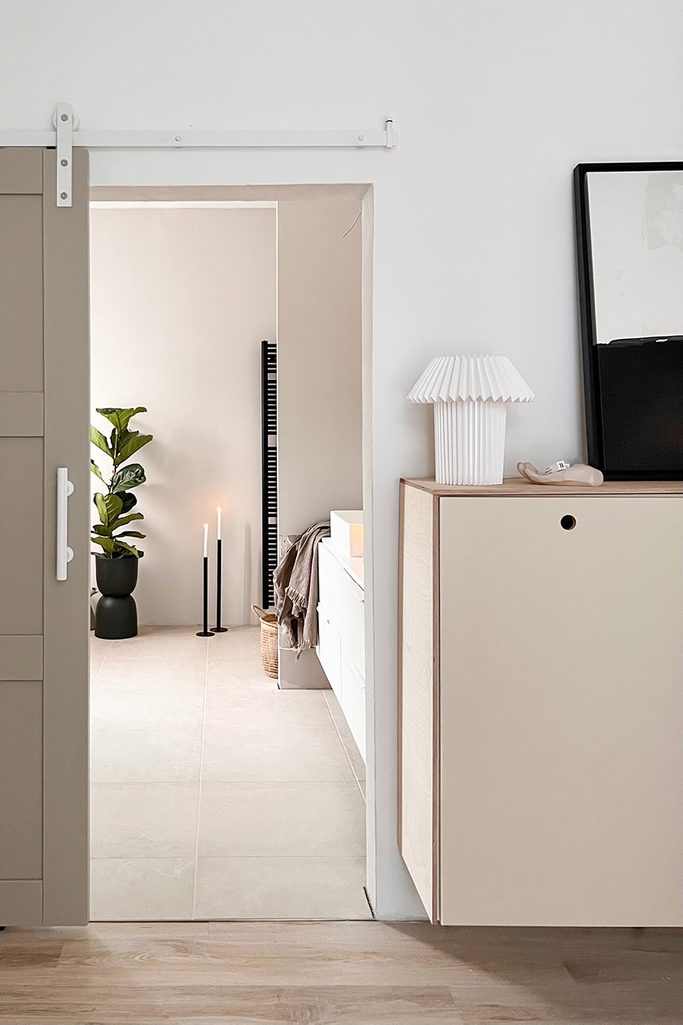 wejście do łazienki urządzonej w szaro-beżowych kolorach z czarnymi akcesoriami