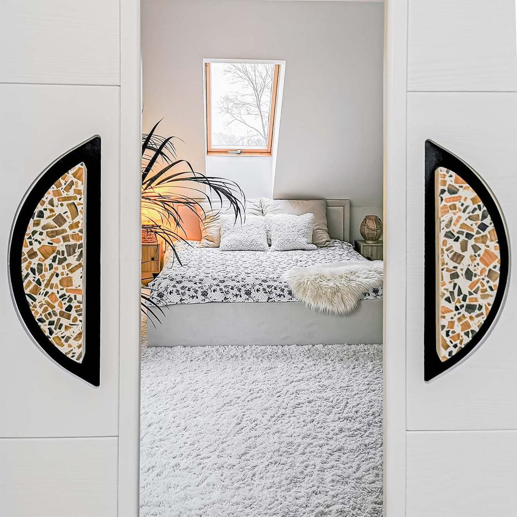 uchylone drzwi ukazujące sypialnię z tapicerowanym łóżkiem w kolorach bieli i beżu